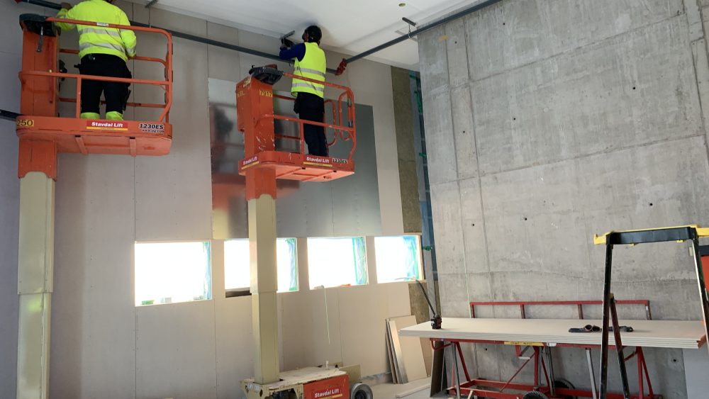 Byggarbetare jobbar på två liftar med att montera innertak. Foto.